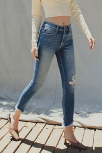 Cotton blend medium wash stretch high rise ankle skinny with fray bottom detail. Subtle distressing on knee area.